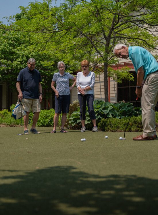 man with golf club on putting green an group watching him