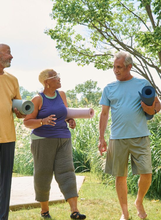 3 people outside walking and talking with yoga mats